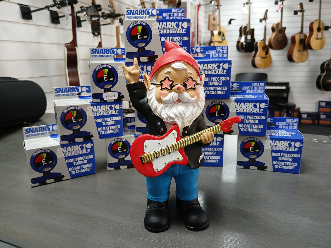 Metro Gnome figurine holding a red guitar surrounded by Snark 1 tuner boxes at Music Bits