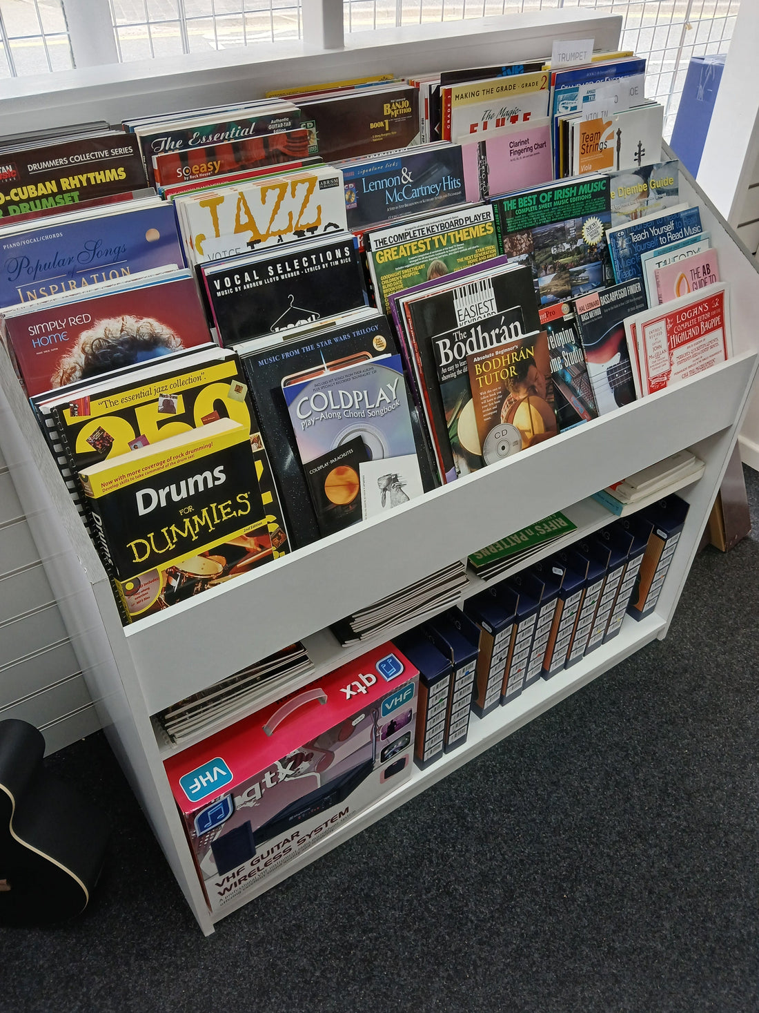 A well-stocked display of sheet music books and music tutors in a music shop, including titles for drums, guitar, jazz, Irish music, and more.